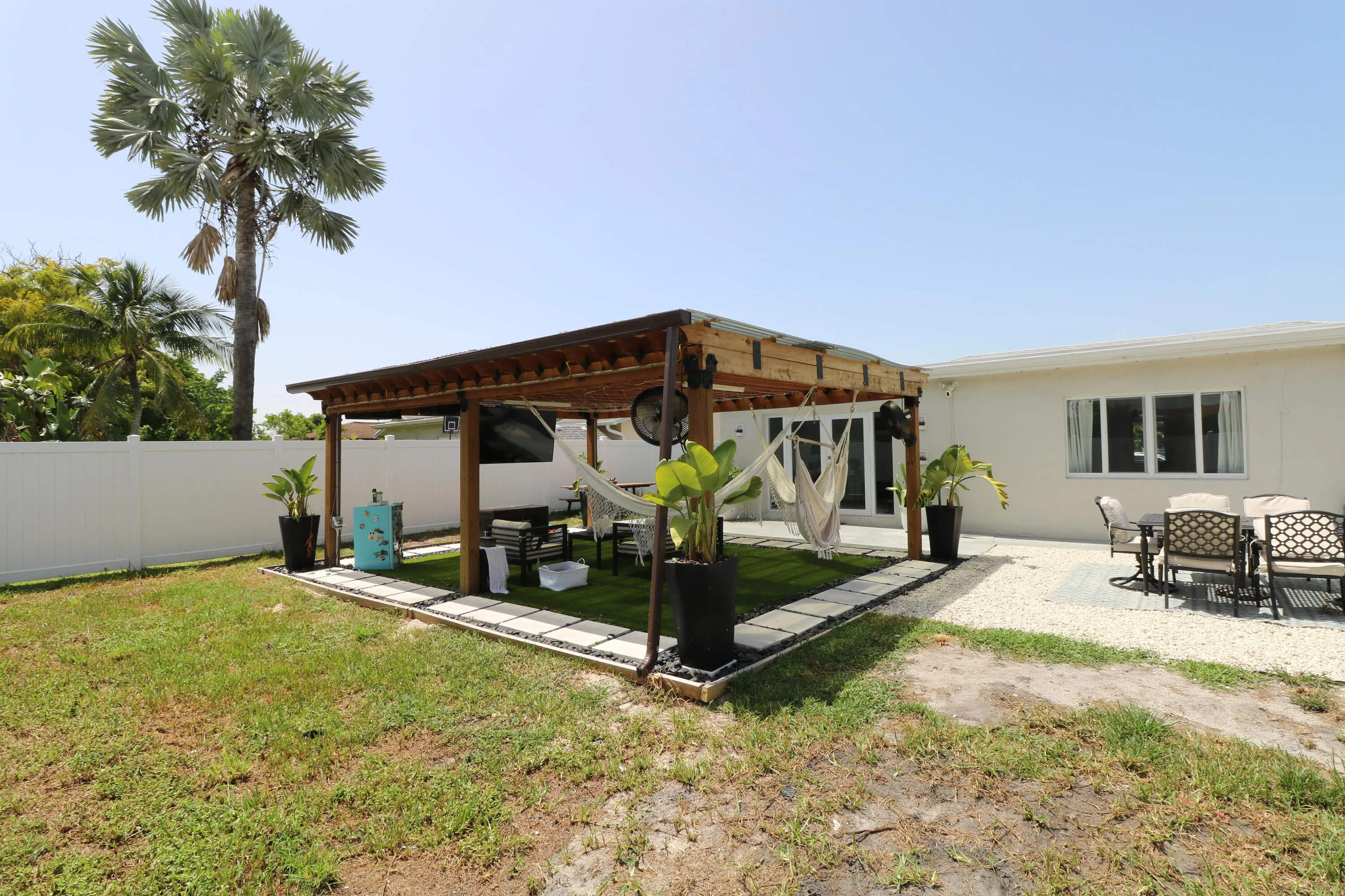 Expansive backyard featuring a pergola with a wood frame and metal roof, a white vinyl fence, a gravel patio, and a manicured lawn