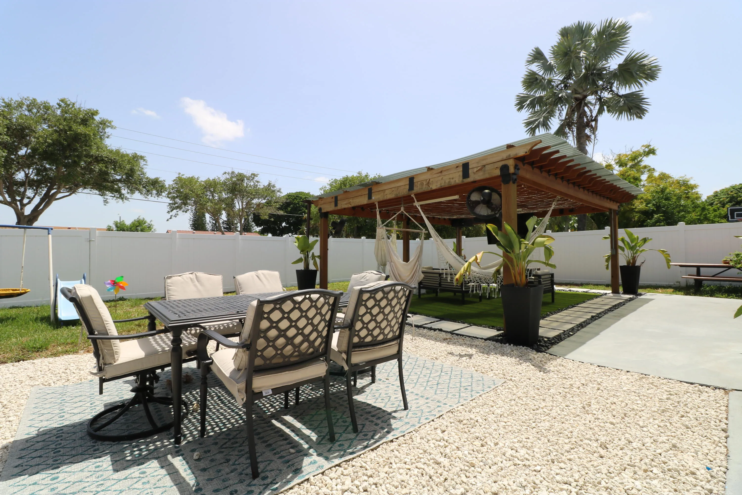 Expansive outdoor space featuring a wood pergola with a corrugated roof, white privacy fencing, and a combination of pea gravel, artificial turf, and concrete surfacing