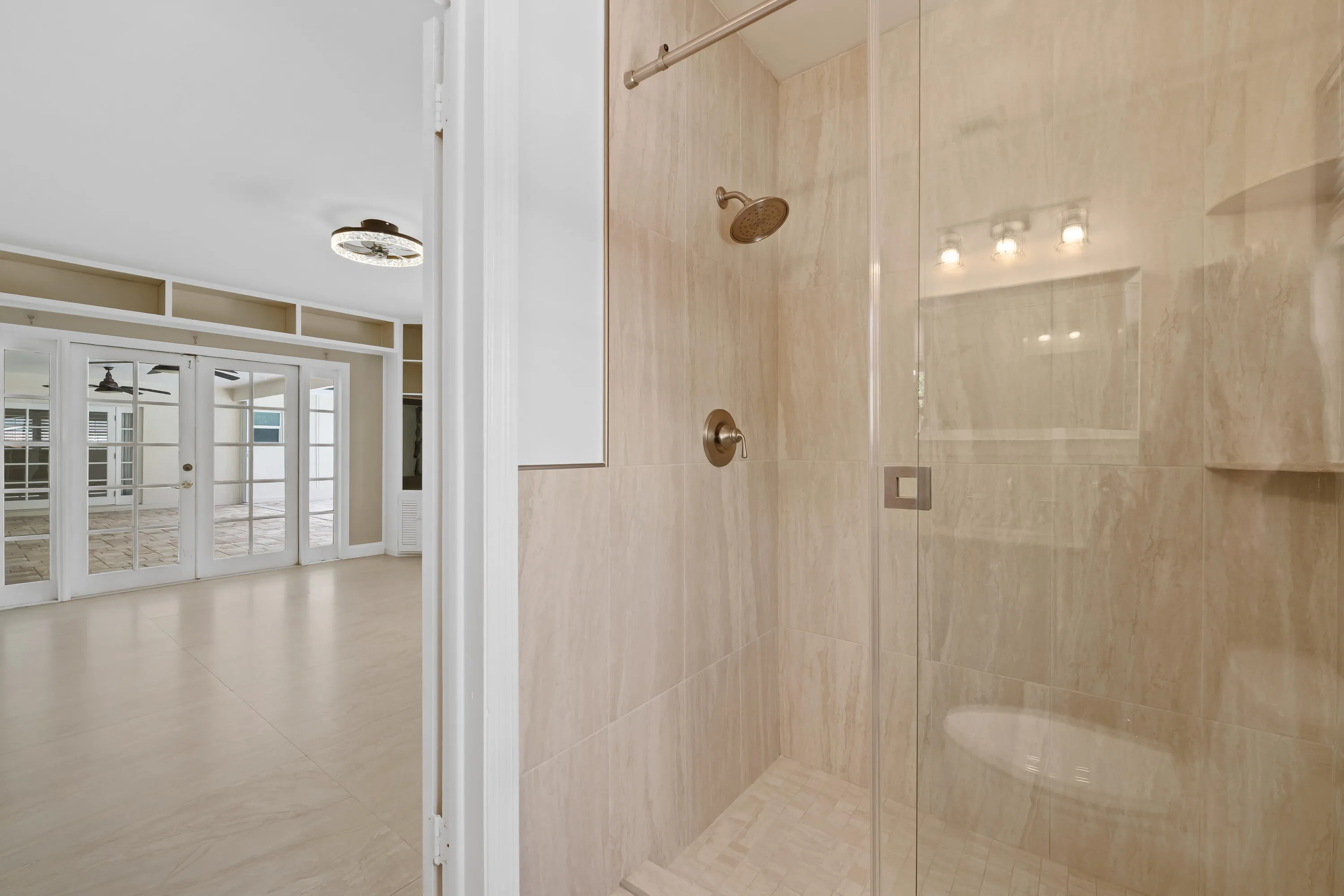 Glass-enclosed shower with a brushed nickel rain showerhead and coordinating fixtures, featuring a recessed niche and light-toned tile surround