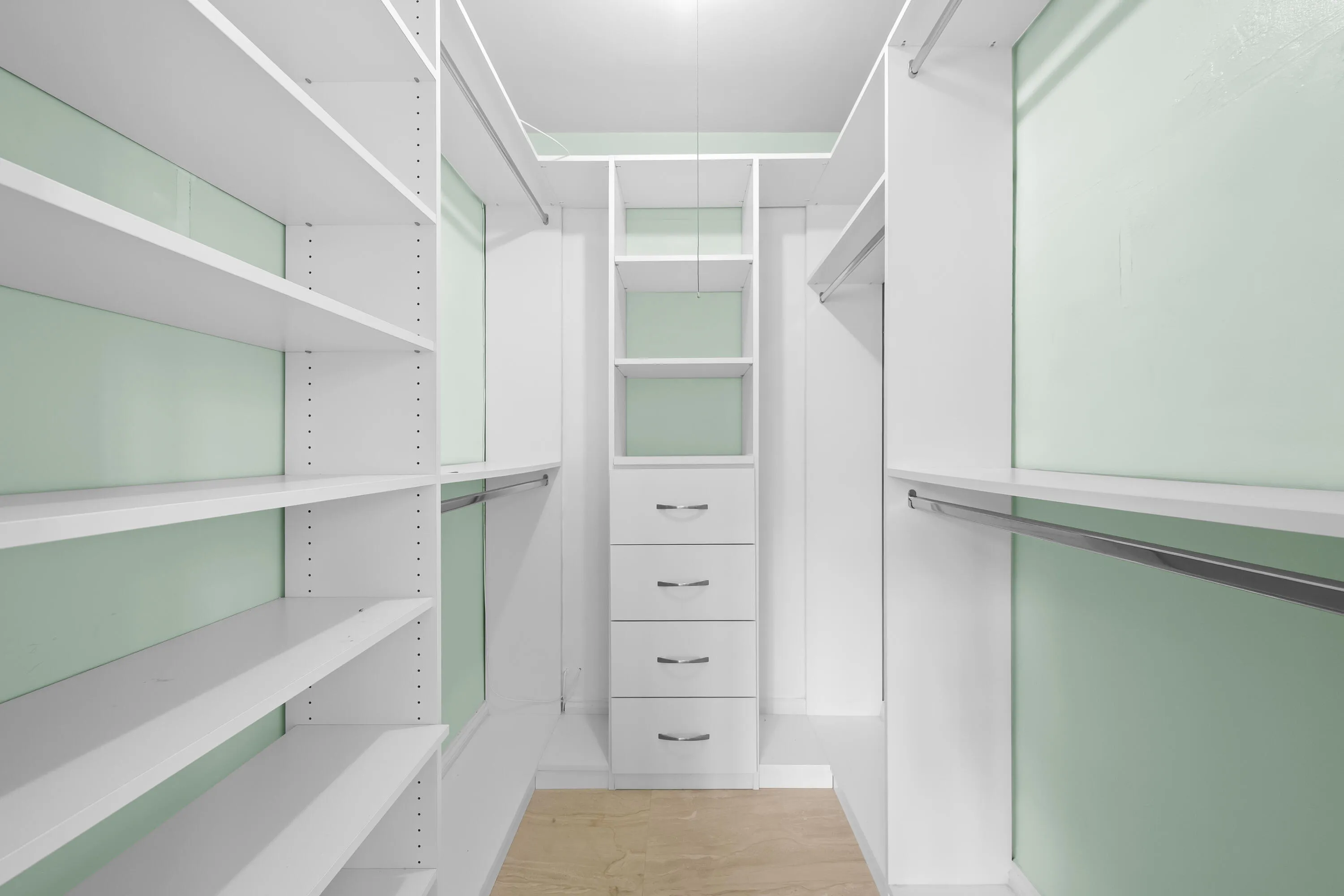 Walk-in closet featuring built-in white shelving, multiple hanging rods, a central storage unit with drawers.