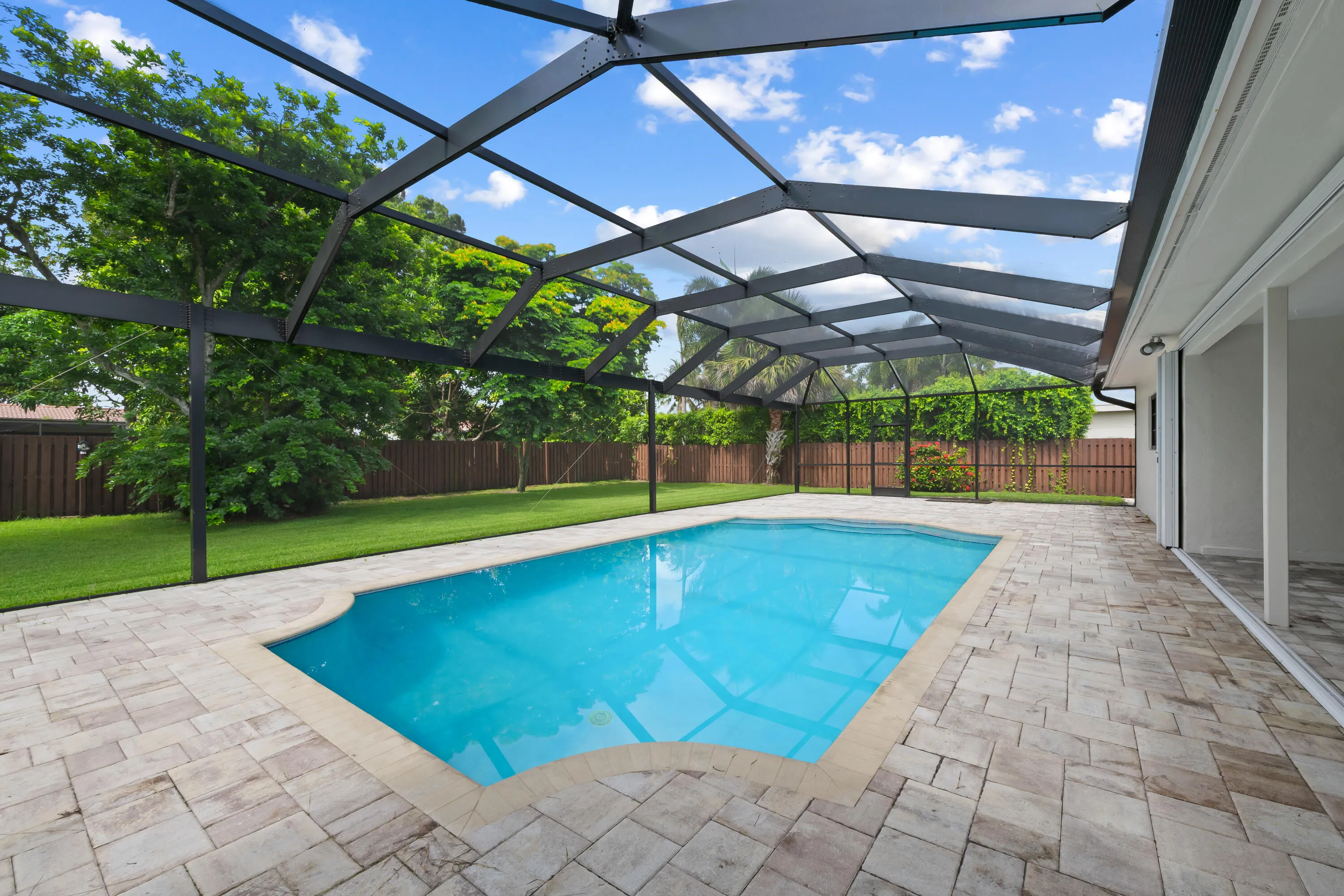 Screened-in outdoor living space featuring an updated swimming pool, expansive paver patio, privacy fence, and mature landscaping.