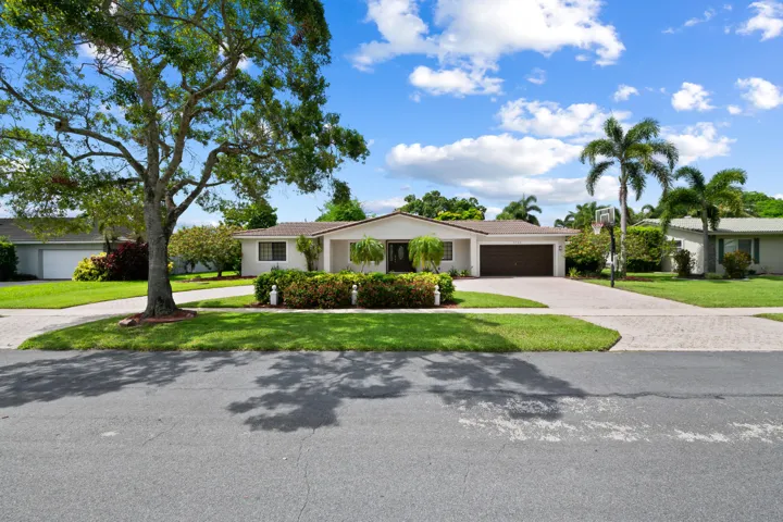 Single-story residence featuring a two-car garage, mature landscaping, paved driveway, and established palm trees
