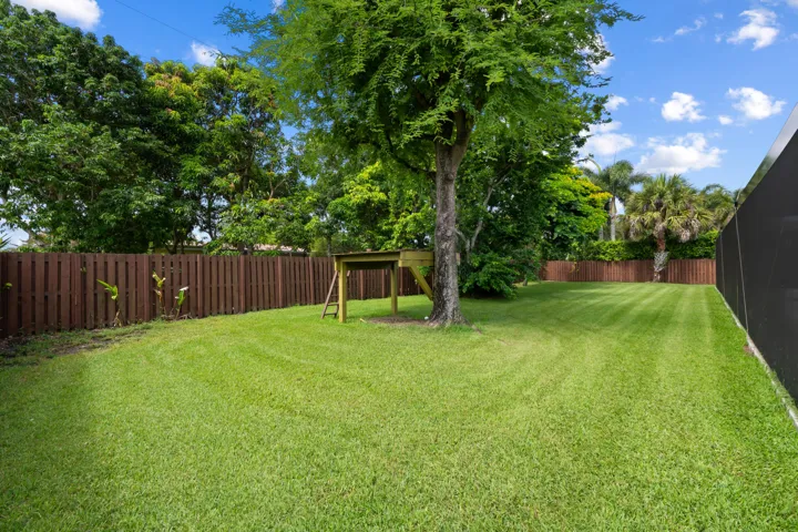 Spacious green lawn featuring a large mature tree and full perimeter fencing.