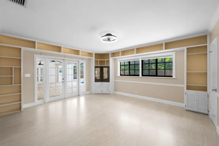 Spacious interior featuring light-toned tile flooring, extensive built-in shelving, a corner built-in cabinet, and large glass French doors opening to an outdoor area.