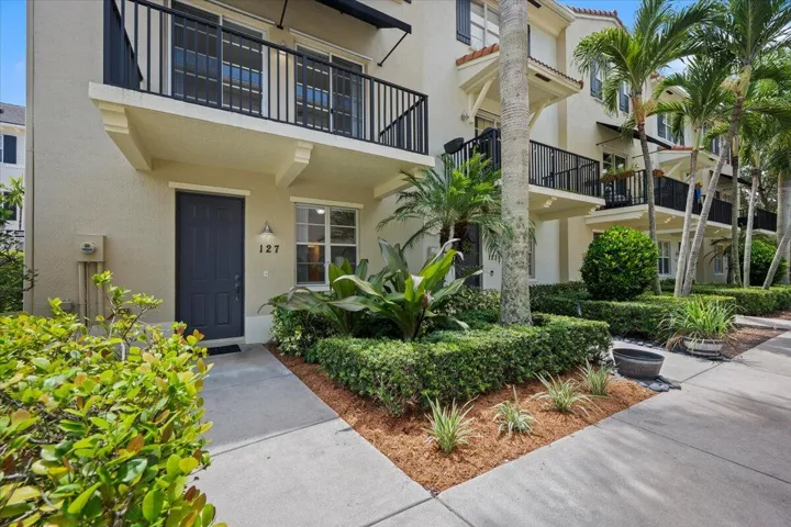 Multi-story stucco exterior featuring black window shutters, a black front door, and a second-story balcony with black railings