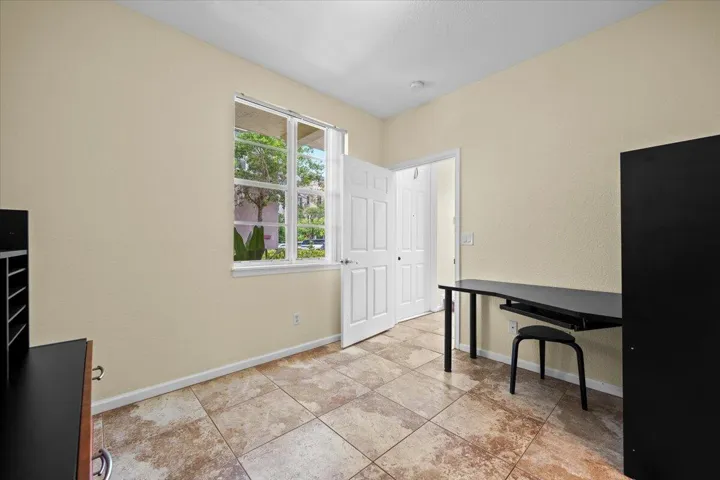 Spacious room featuring neutral-toned walls, a large window, tiled flooring, and a white paneled door