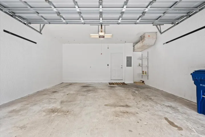 Spacious garage featuring a concrete floor, exposed ceiling joists, and a white interior door