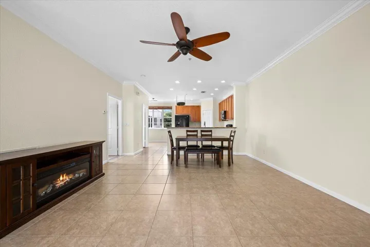 Spacious open-concept living area featuring large format tile flooring, crown molding, and a ceiling fan