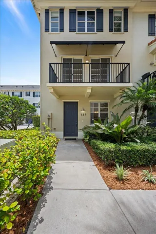 Stucco exterior featuring dark shutters, a second-story balcony with iron railings, and a ground-level entrance with a dark paneled door