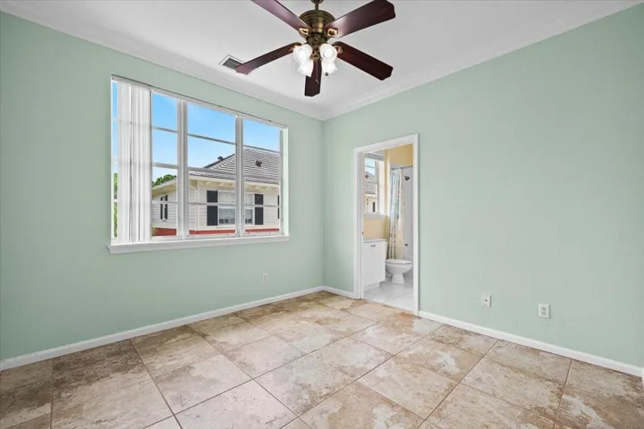 Spacious room featuring tile flooring, a large multi-pane window, crown molding, and a ceiling fan with integrated lighting