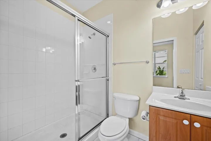 Full bathroom featuring a walk-in shower with sliding glass doors, white tile surround, and a wood-finish vanity with an integrated sink and chrome fixtures