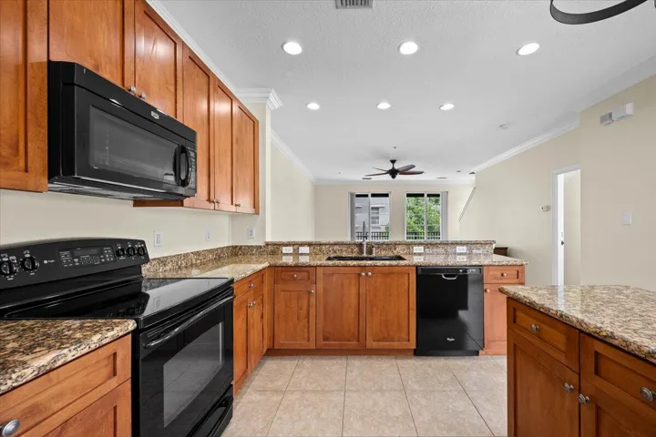 Well-appointed kitchen featuring wood cabinetry, granite countertops, tile flooring, and integrated black appliances