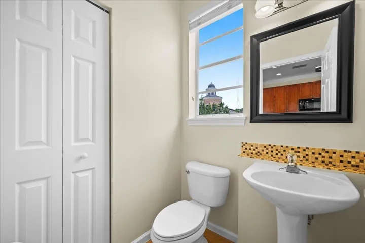 Bathroom featuring a pedestal sink with a mosaic tile backsplash, a toilet, and a window
