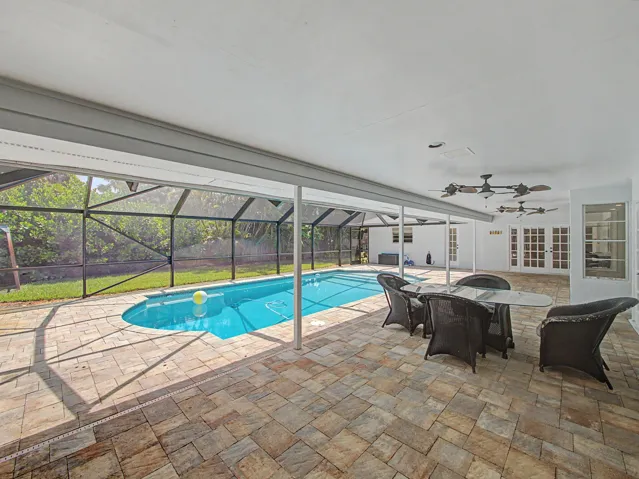 Screened enclosure featuring a swimming pool, paver patio, and multiple ceiling fans