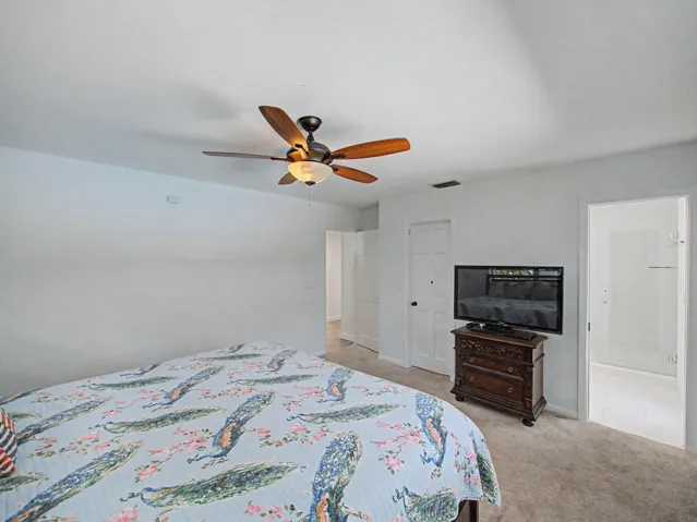 Carpeted bedroom featuring a ceiling fan with light fixture, white walls, and a white paneled door