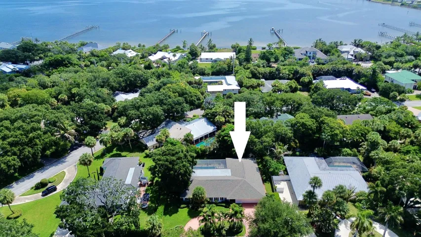 Aerial perspective showcasing a single-story residence with a light-colored roof surrounded by mature trees