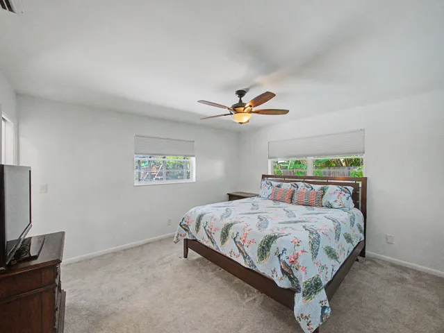 Spacious room featuring light-colored carpeting, two windows with white blinds, and a ceiling fan with integrated lighting