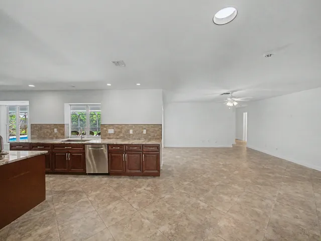 Expansive open-concept living area featuring a kitchen with wood-finish cabinetry, stainless steel appliances, a stone-finish backsplash, and a breakfast bar