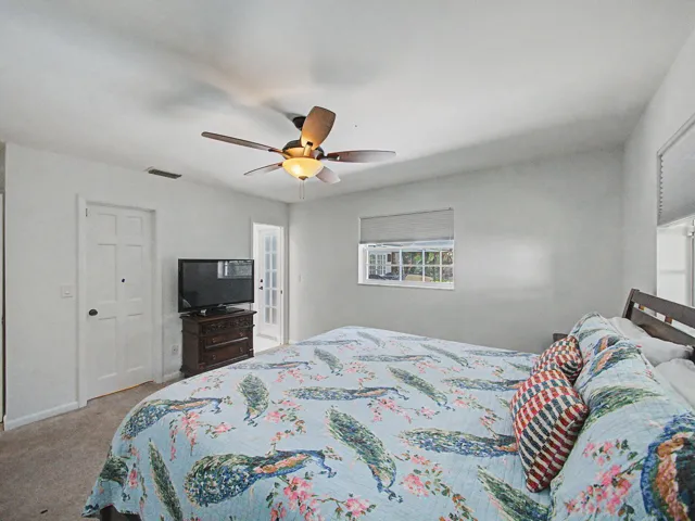 Bedroom featuring a ceiling fan with integrated lighting, a window with exterior visibility, and a paneled door
