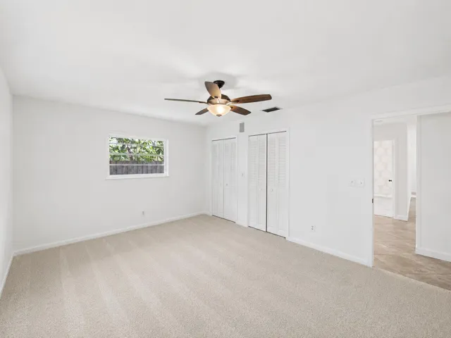 Neutral-toned carpeted flooring, white walls, and a ceiling fan with integrated lighting