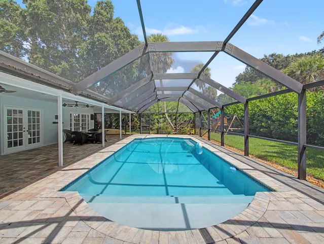 Screened pool enclosure featuring a rectangular swimming pool with integrated steps, surrounded by stone paver decking