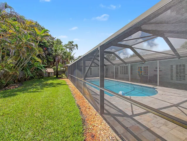 Screened swimming pool with a paver deck, surrounded by mature tropical landscaping and a manicured lawn