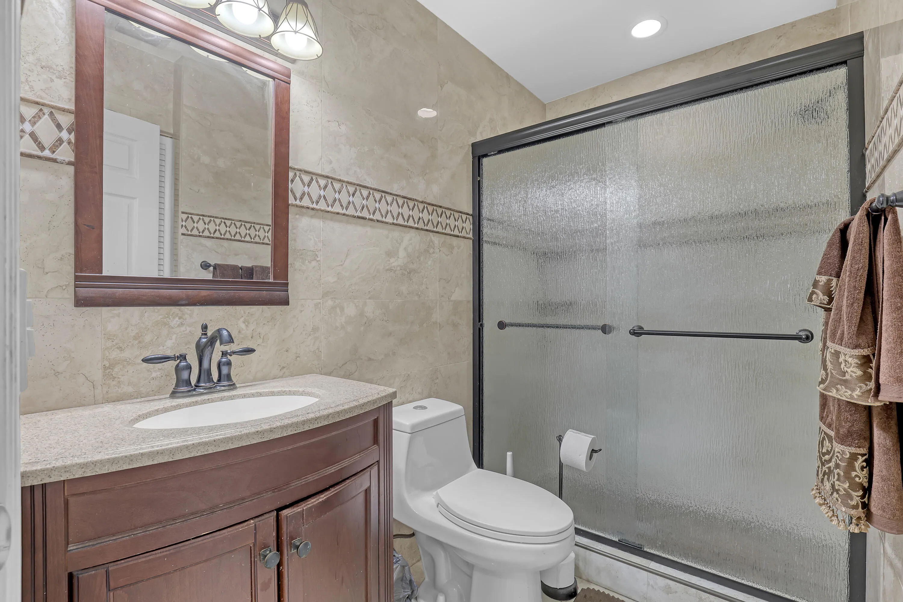Full bathroom featuring a dark wood-finish vanity with a light countertop, a framed mirror, and a glass-enclosed shower
