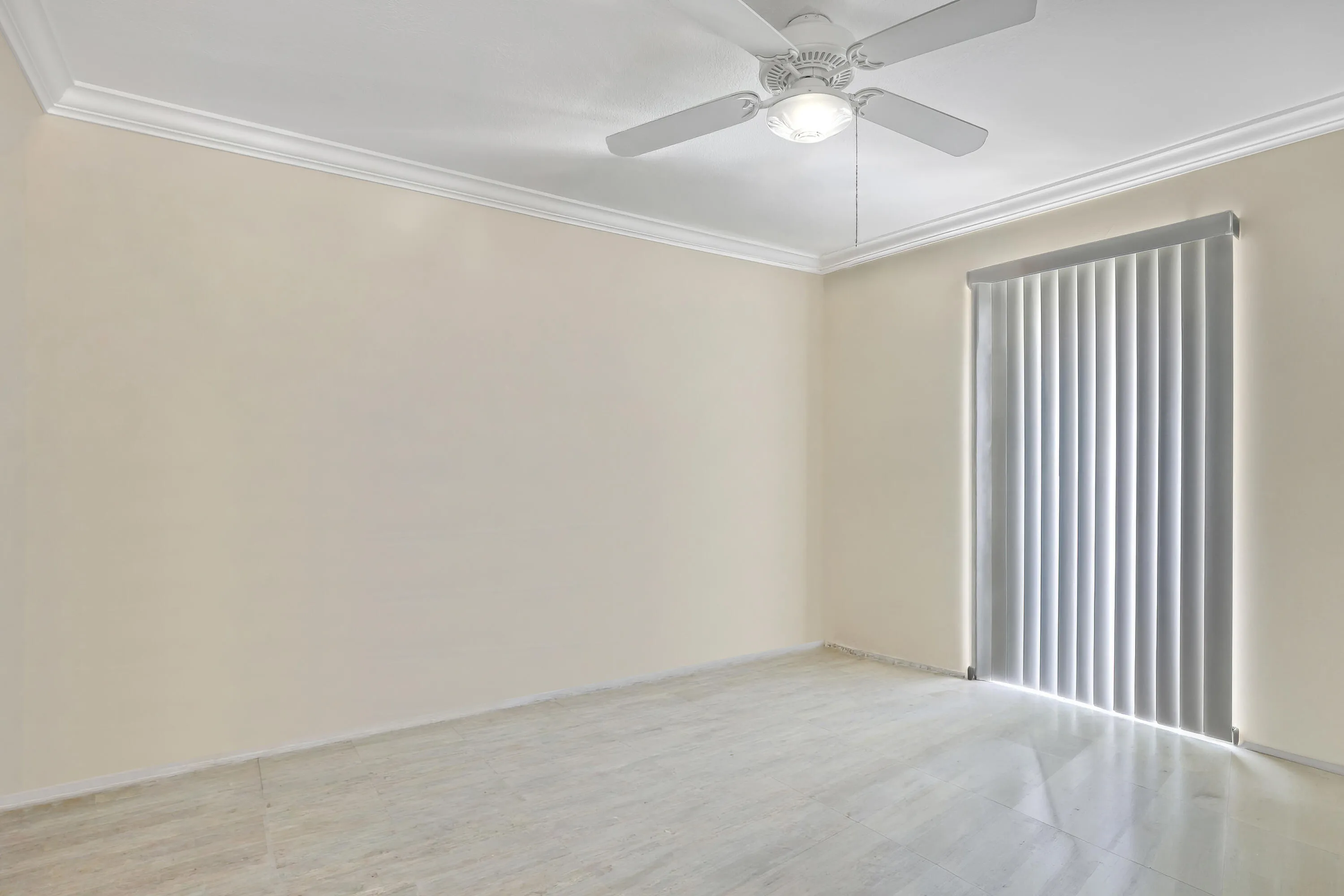 Room featuring pale neutral walls, crown molding, a ceiling fan with integrated lighting, a large window with vertical blinds, and light-toned tile flooring