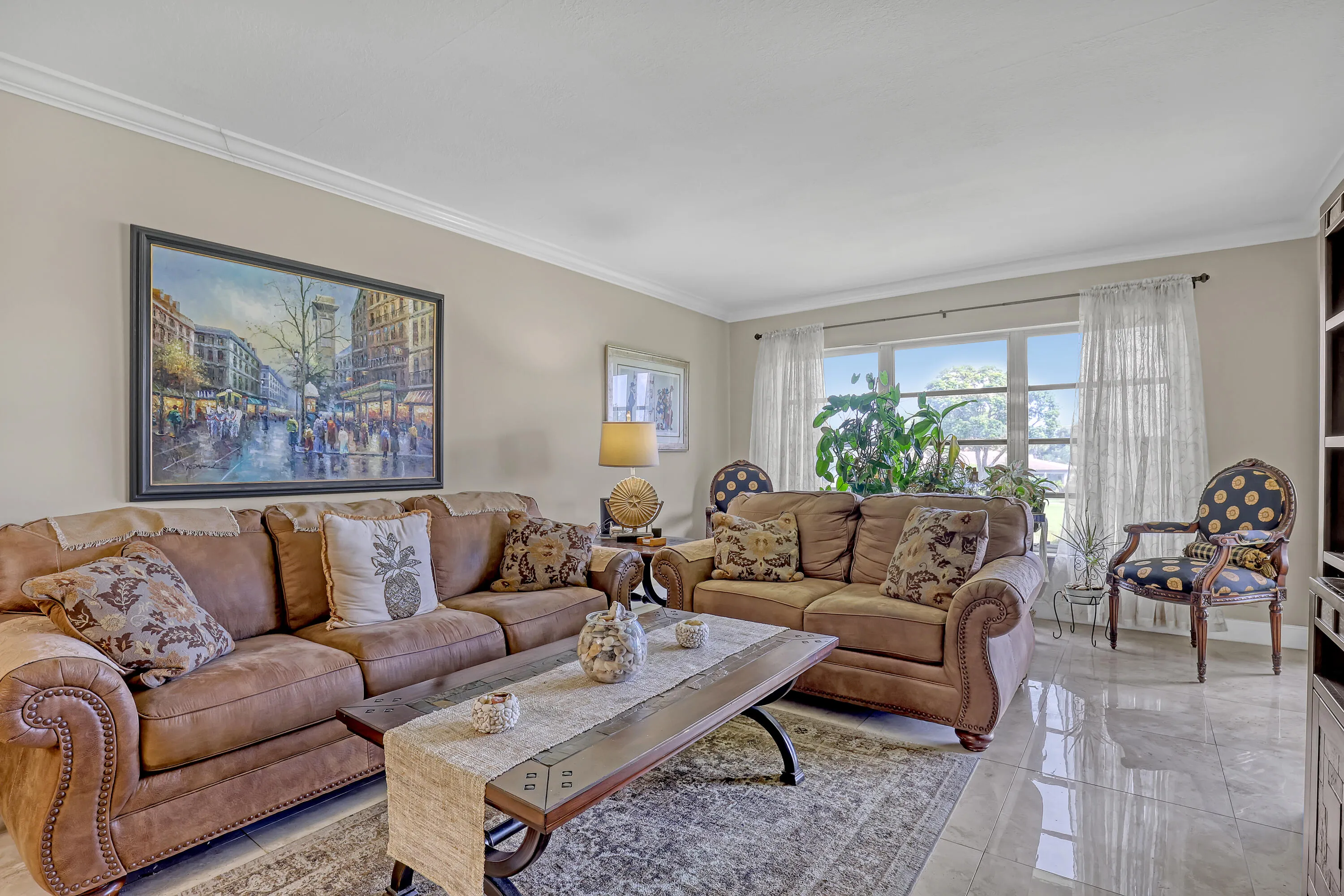 Spacious living area featuring polished tile flooring, crown molding, a large picture window, and neutral wall tones