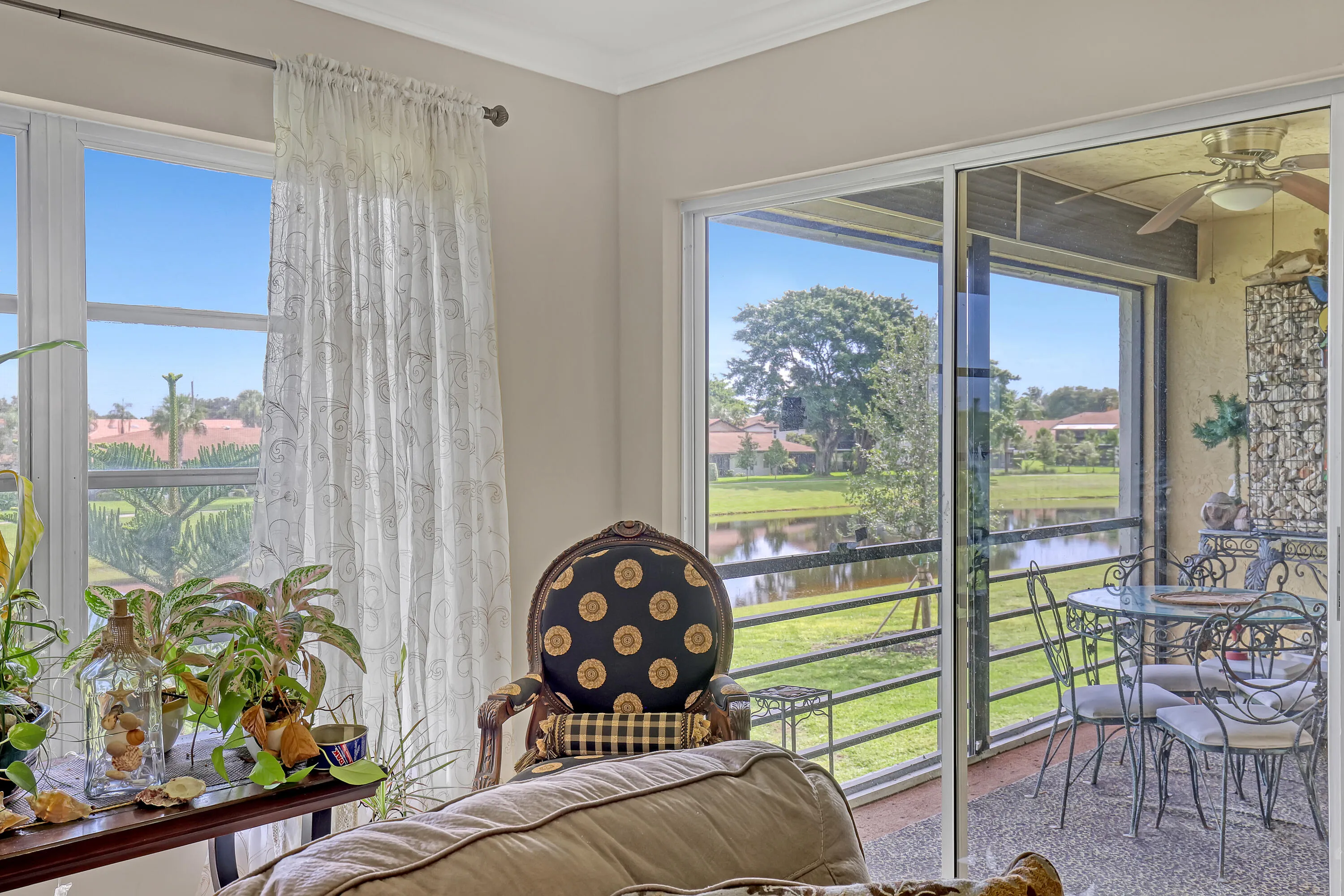 Sliding glass doors opening to a screened porch with a ceiling fan, offering views of a pond and green space