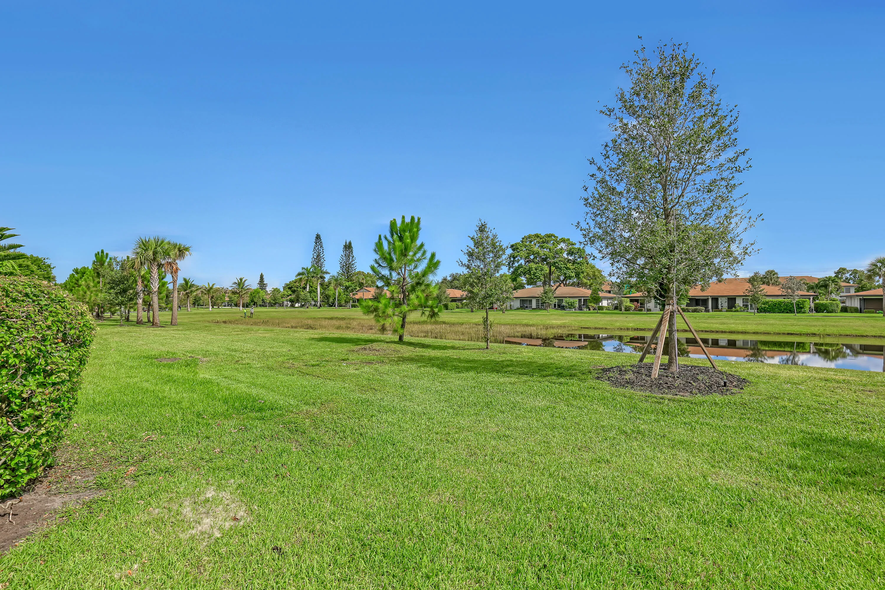 Expansive green space featuring a tranquil water body, established trees, and surrounding residences with terracotta-style roofing
