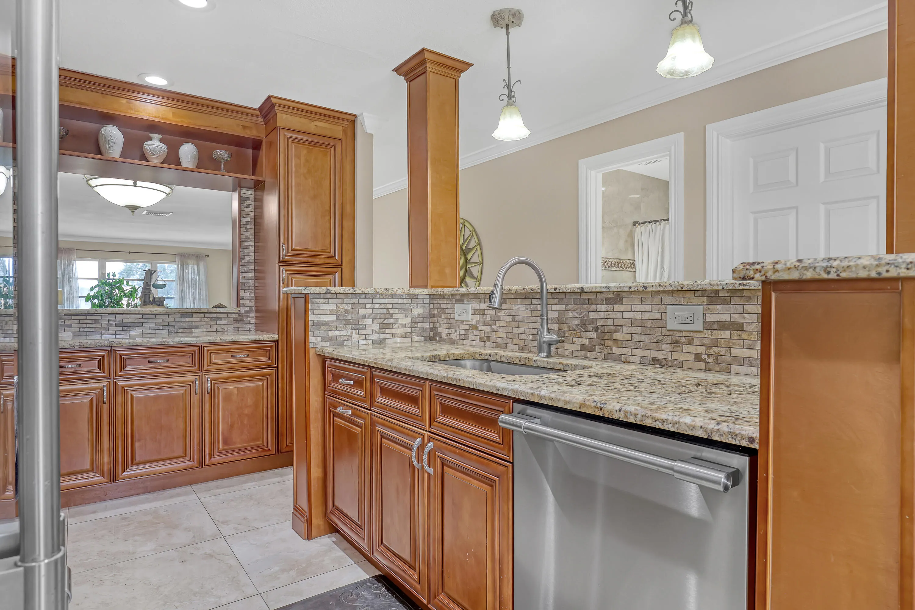 Kitchen area featuring rich wood cabinetry, granite countertops, a mosaic tile backsplash, stainless steel appliances, and tile flooring