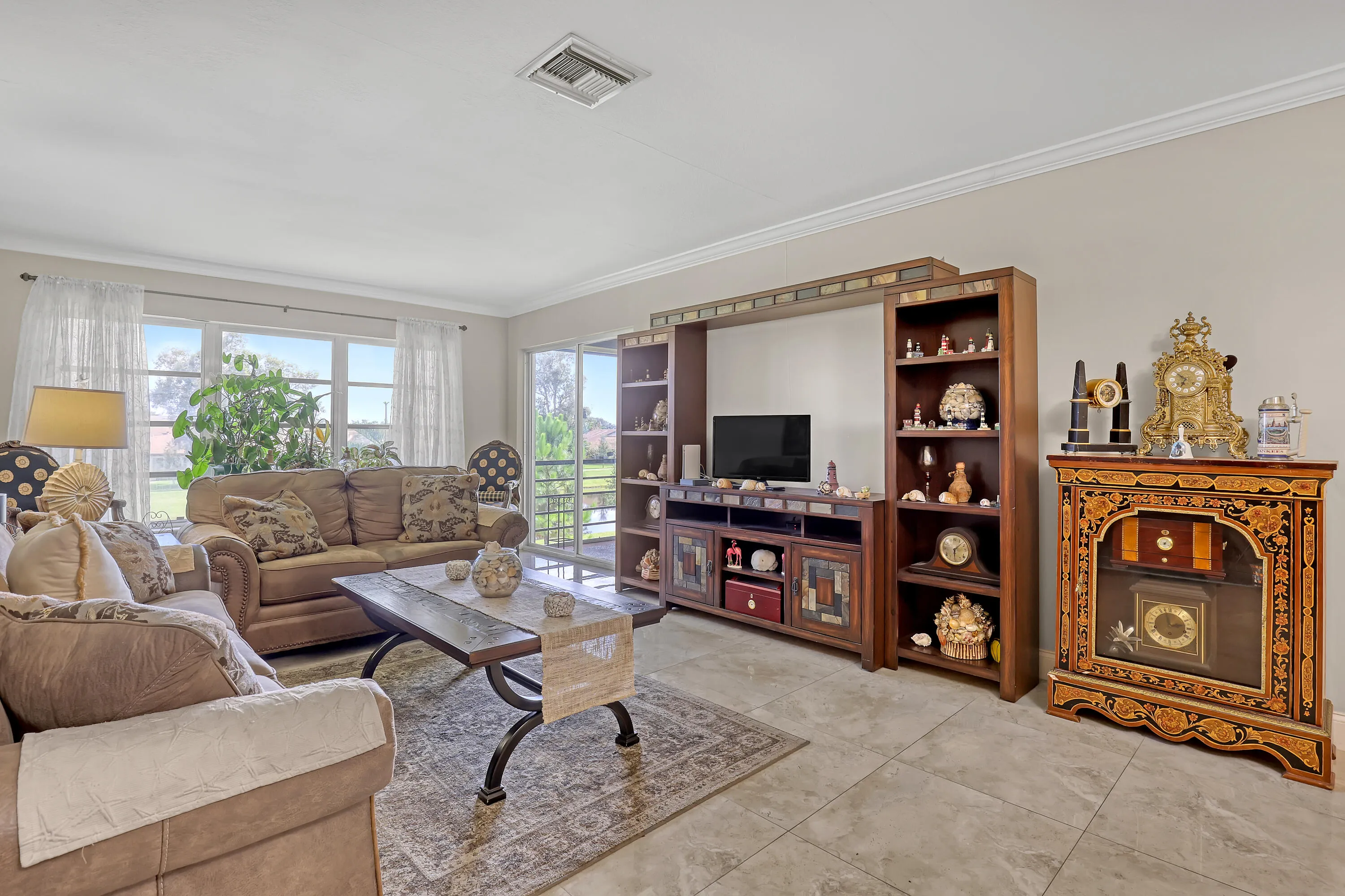 Spacious living area featuring neutral wall tones, crown molding, and large format tile flooring