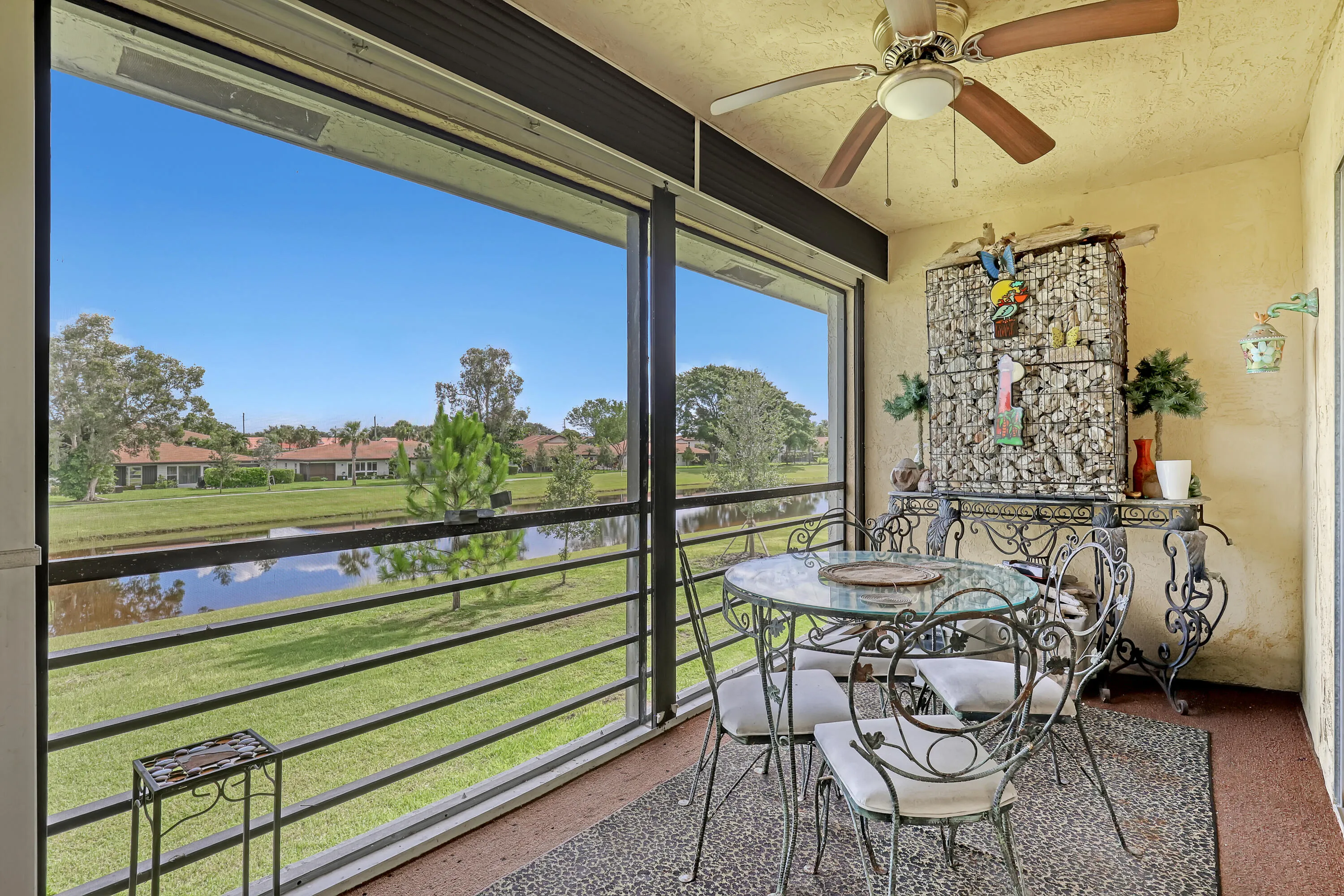 Screened lanai featuring textured walls, an overhead ceiling fan with lighting, and a panoramic water and green space outlook