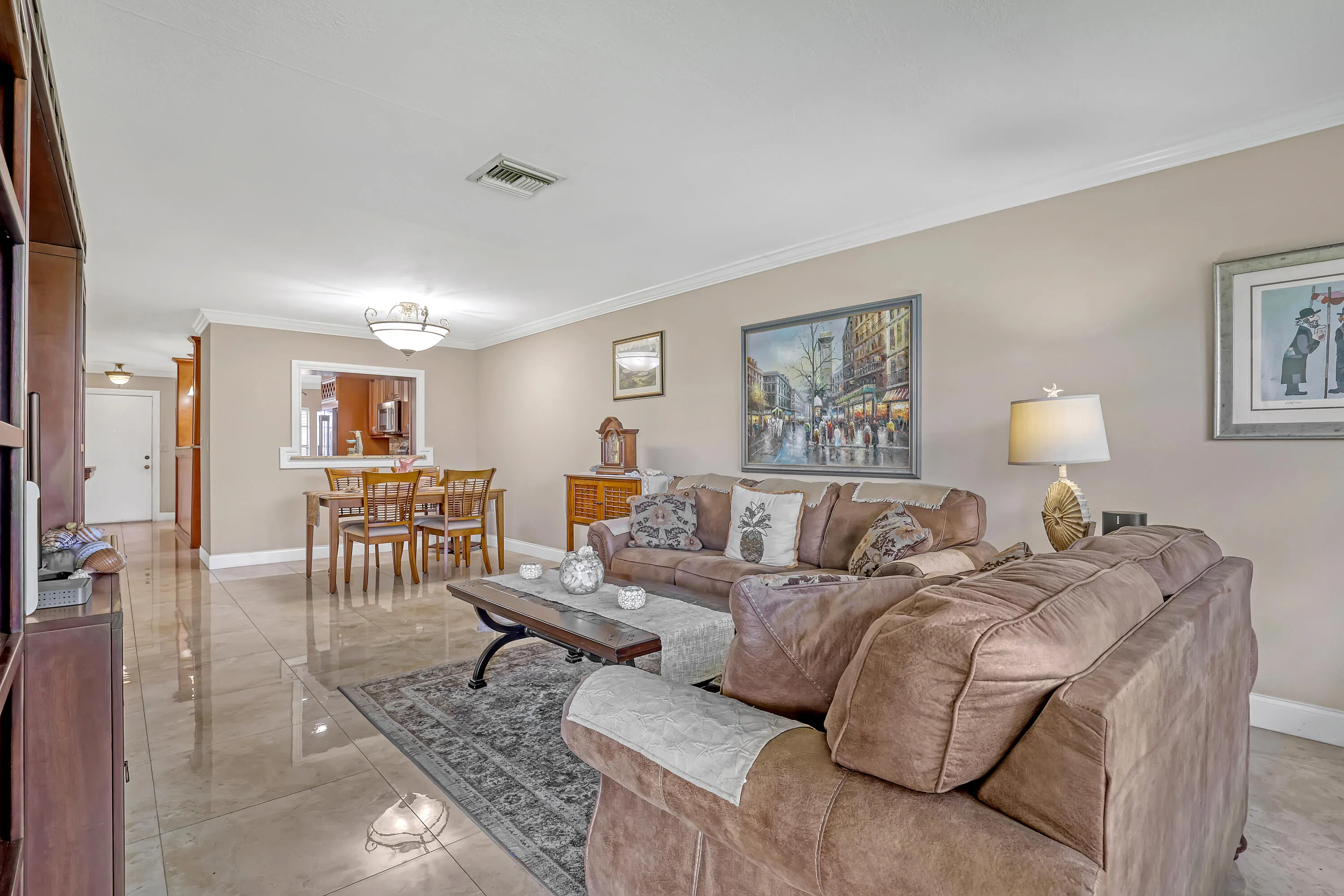 Spacious living area featuring polished tile flooring, neutral wall tones, and crown molding