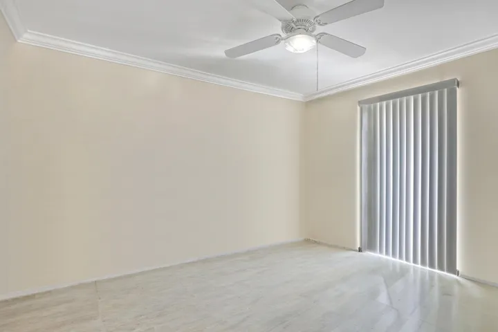Room featuring pale neutral walls, crown molding, a ceiling fan with integrated lighting, a large window with vertical blinds, and light-toned tile flooring