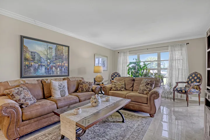 Spacious living area featuring polished tile flooring, crown molding, a large picture window, and neutral wall tones