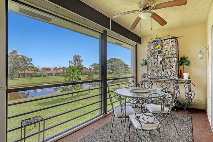Screened lanai featuring textured walls, an overhead ceiling fan with lighting, and a panoramic water and green space outlook