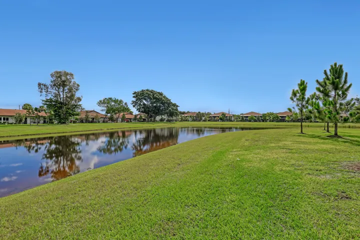 Expansive green space with a water feature, bordered by mature trees and residential properties