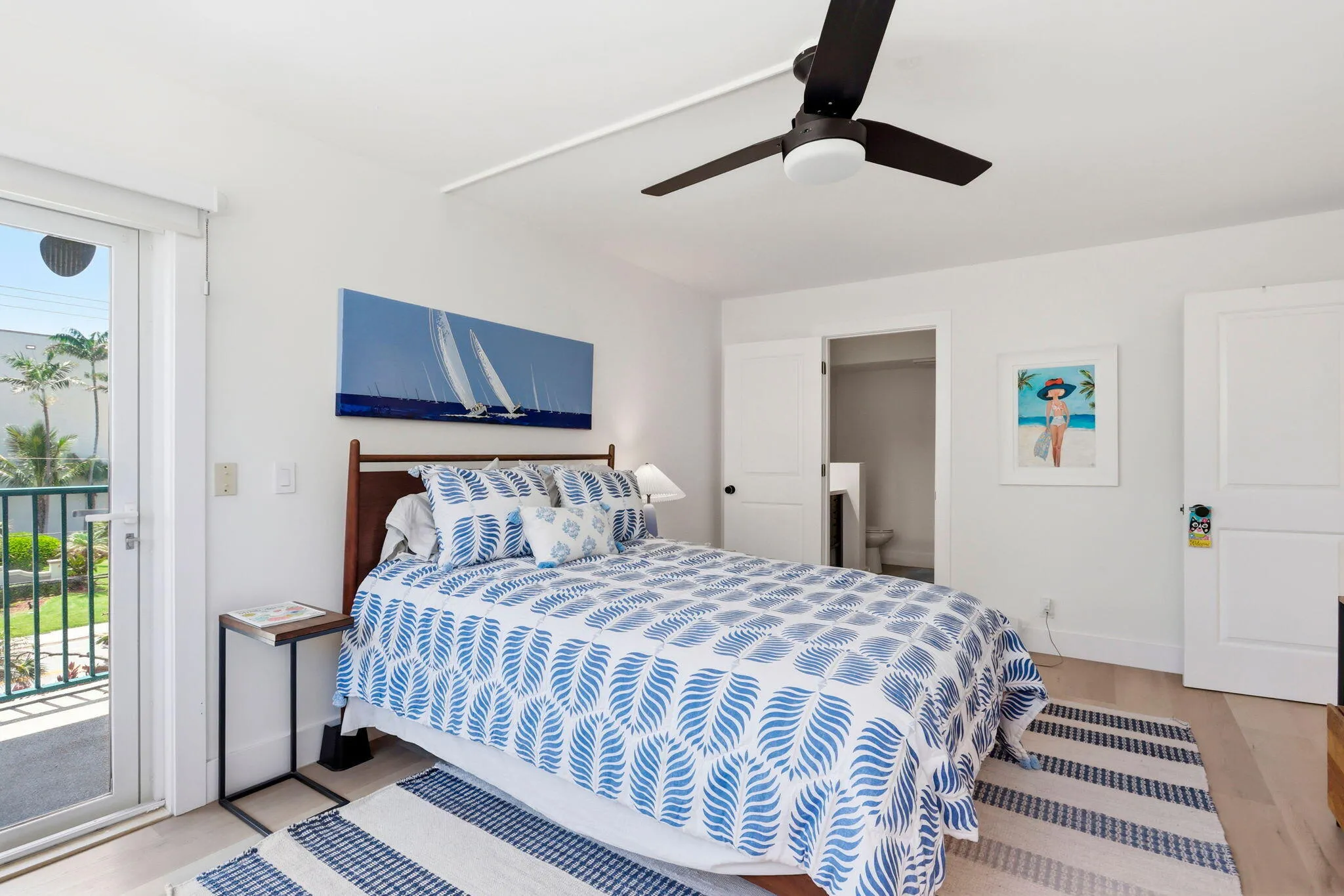 Light wood-finish flooring complements white walls in this bedroom, featuring a glass-paneled door opening to a balcony with views of the intracoastal and sunsets!
