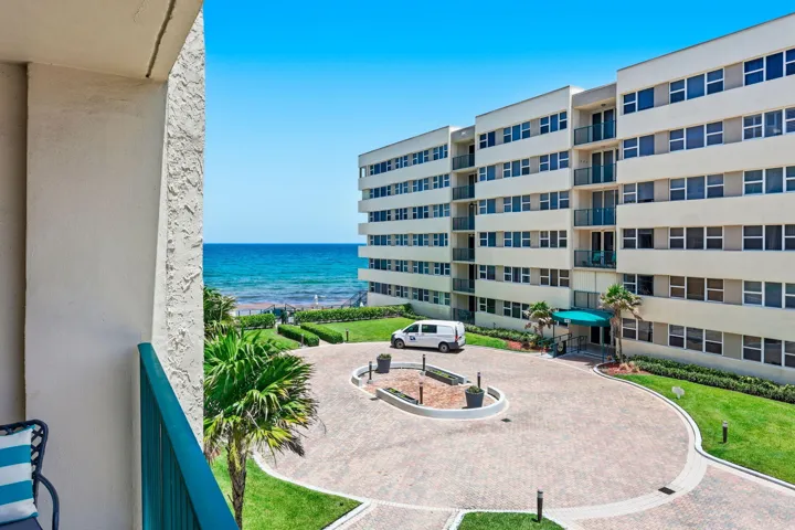 Oceanfront building featuring multiple balconies, a circular paver driveway, and a manicured lawn