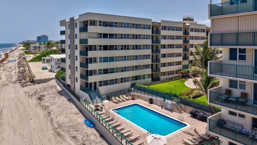 Multi-story building featuring private balconies with green railings, an outdoor swimming pool, and a manicured lawn area