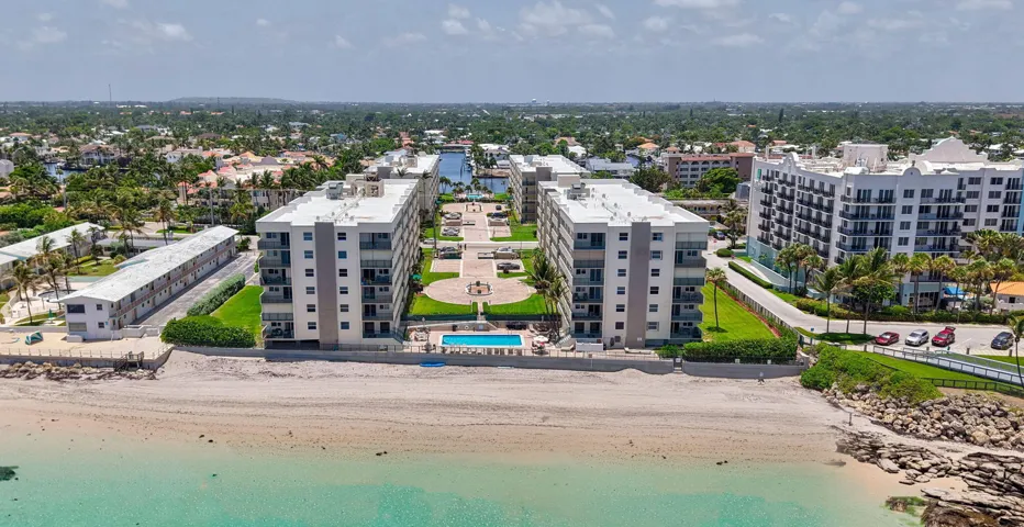 Coastal condominium buildings featuring private balconies, a swimming pool, manicured green spaces, and direct beach access