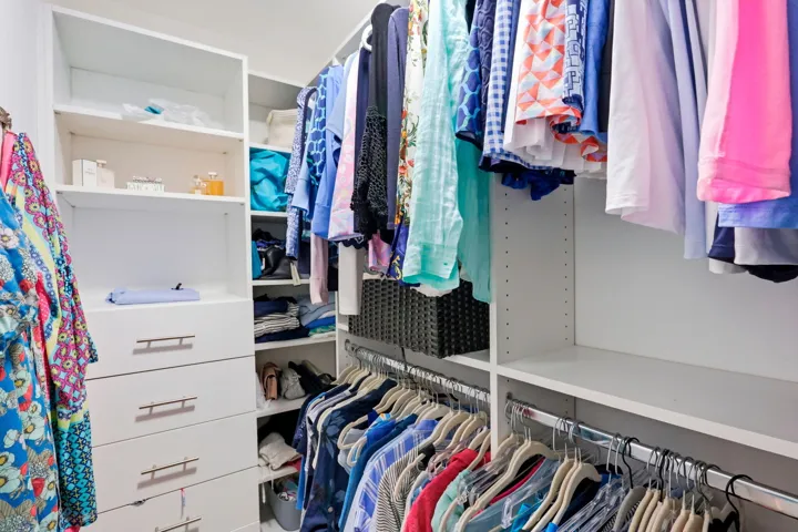 Custom closet system featuring white shelving, multiple hanging rods, built-in drawers with brushed nickel hardware, and varied storage compartments