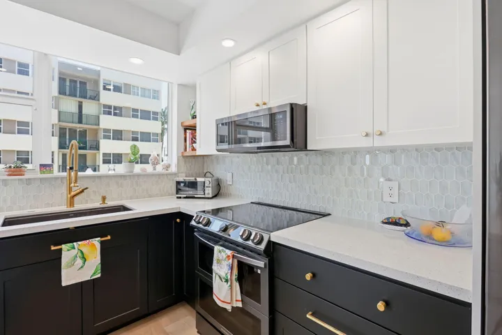 Modern kitchen with two-tone cabinetry, light-toned countertops, and a full-height geometric tile backsplash