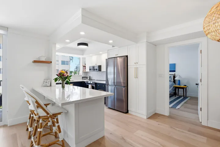 Kitchen featuring white shaker cabinetry, stainless steel appliances, light luxury vinyl flooring, and a quartz countertop island with seating
