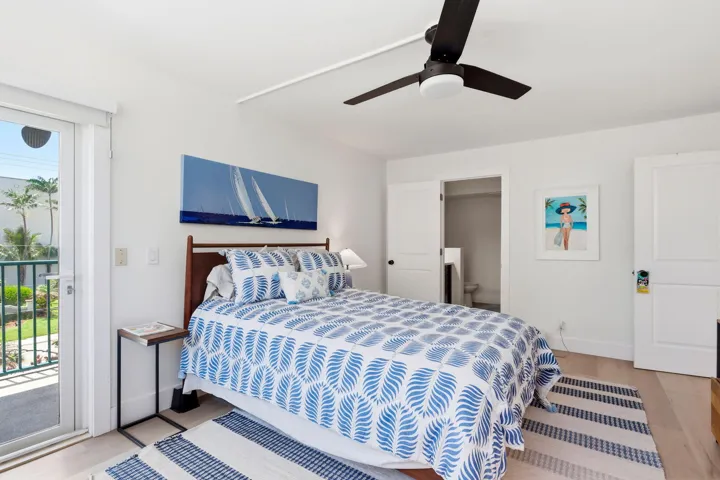 Light wood-finish flooring complements white walls in this bedroom, featuring a glass-paneled door opening to a balcony with views of the intracoastal and sunsets!