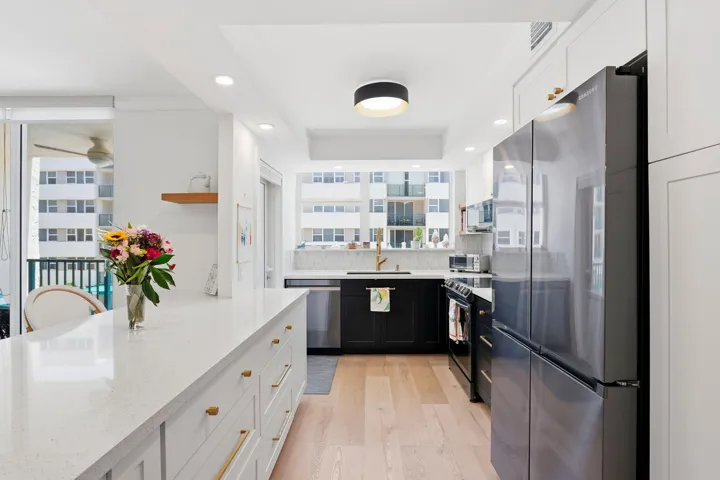 Modern kitchen featuring a large white quartz countertop island with gold-finish hardware, stainless steel appliances, light wood-finish flooring, and white and black cabinetry