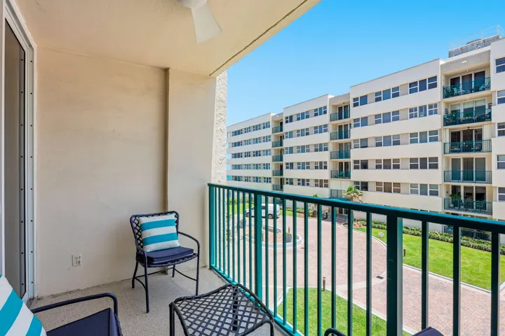 Private balcony featuring a textured stucco finish, a ceiling fan, and black metal railings with a green top rail