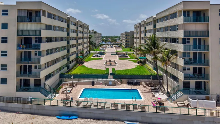Oceanfront resort-style living featuring a large swimming pool, expansive paver deck, and direct beach access